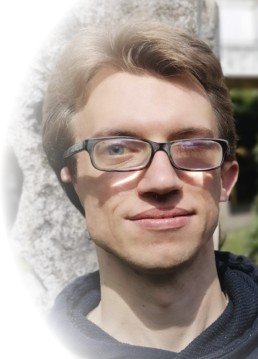 Edvin Duric mit Brille, kurzen dunkelblonden Haaren und leichten Bartstoppeln. Er trägt einen dunklen Hoodie und steht im Freien vor einem Felsen.